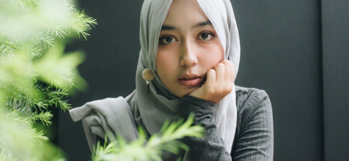 woman wearing gray long-sleeved top and gray hijab right hand on cheek